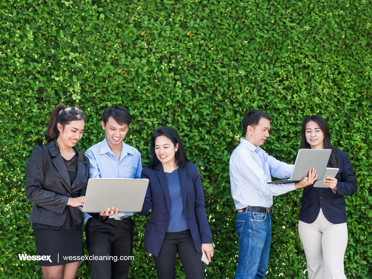 Business people working on laptops in front of a green plant wall, representing an eco-friendly workspace.