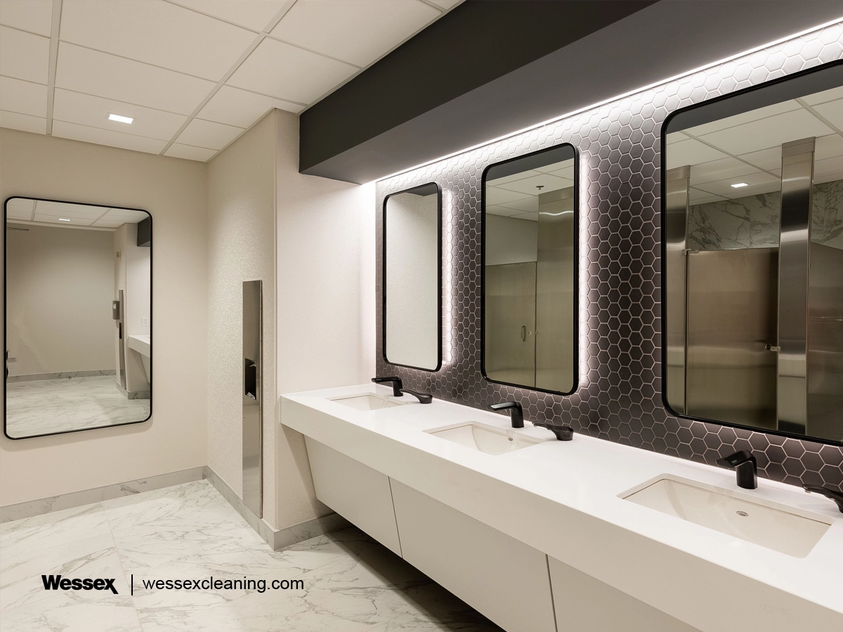 A modern bathroom featuring three white porcelain sinks lined up against a mirrored wall, equipped with smart, touchless faucets for enhanced hygiene.