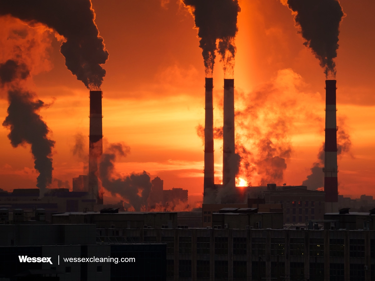 Smoking chimneys of a power plant at sunset, representing industrial greenhouse gas emissions contributing to climate change.