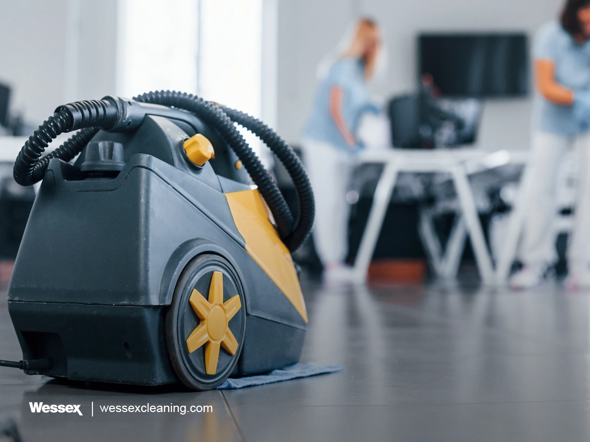 Woman using a vacuum cleaner while a group of workers clean a modern office, highlighting teamwork in green cleaning.