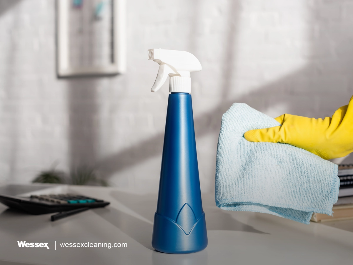Cropped view of person holding cleaning rag near detergent bottle with sprayer on table
