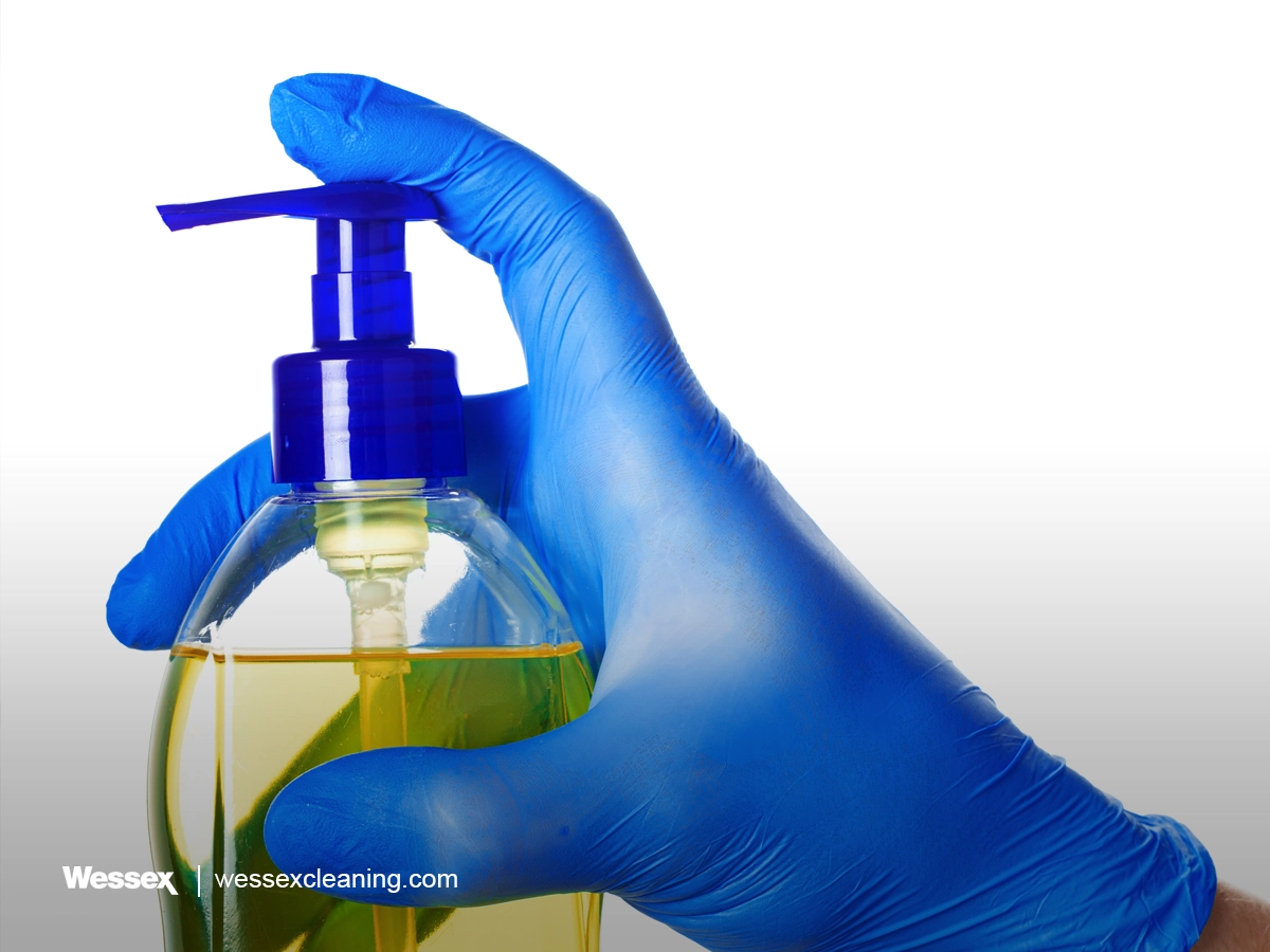 Person wearing blue glove holding a soap bottle on white background